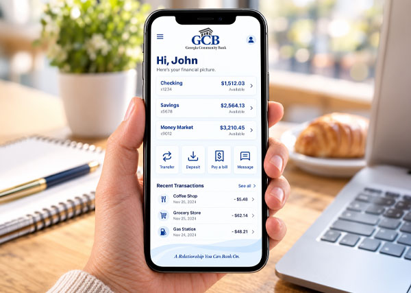 A hand holds a phone which displays the GCB mobile app, with paid bill amounts and transfers showing.